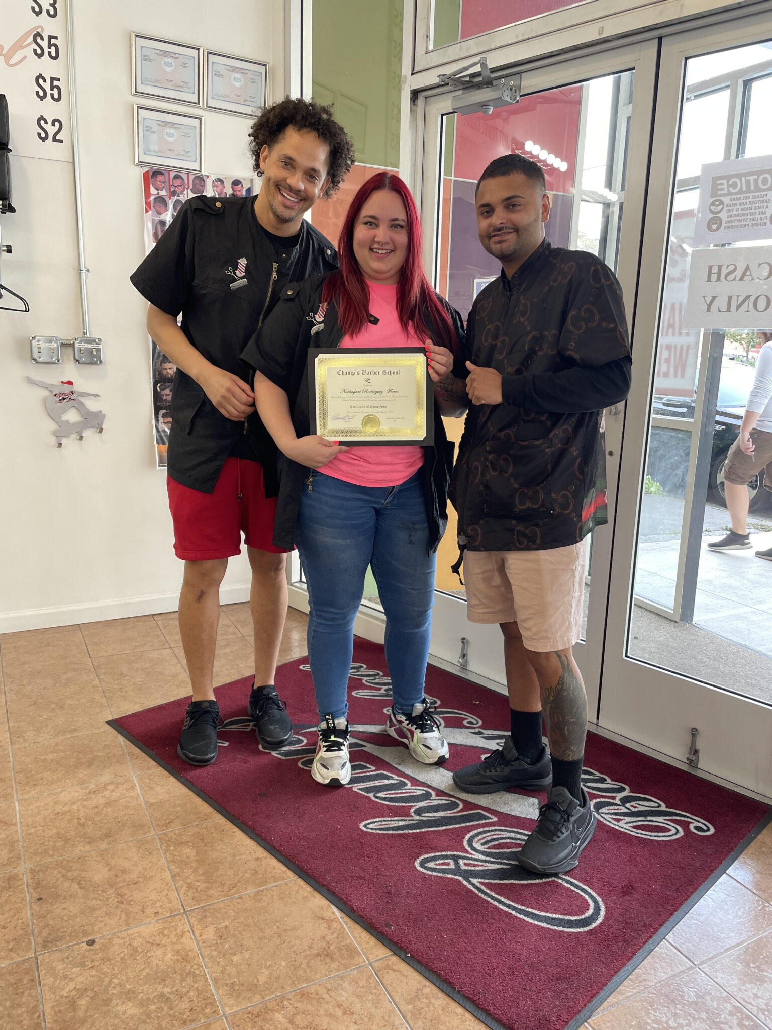 Three people stand smiling inside a shop, one holding a certificate.